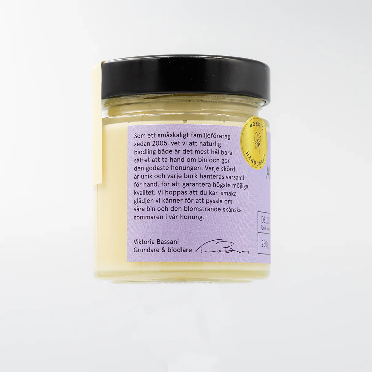 Glasburk med ljus krämig honung, svart lock, etikett med text om naturlig svensk honung