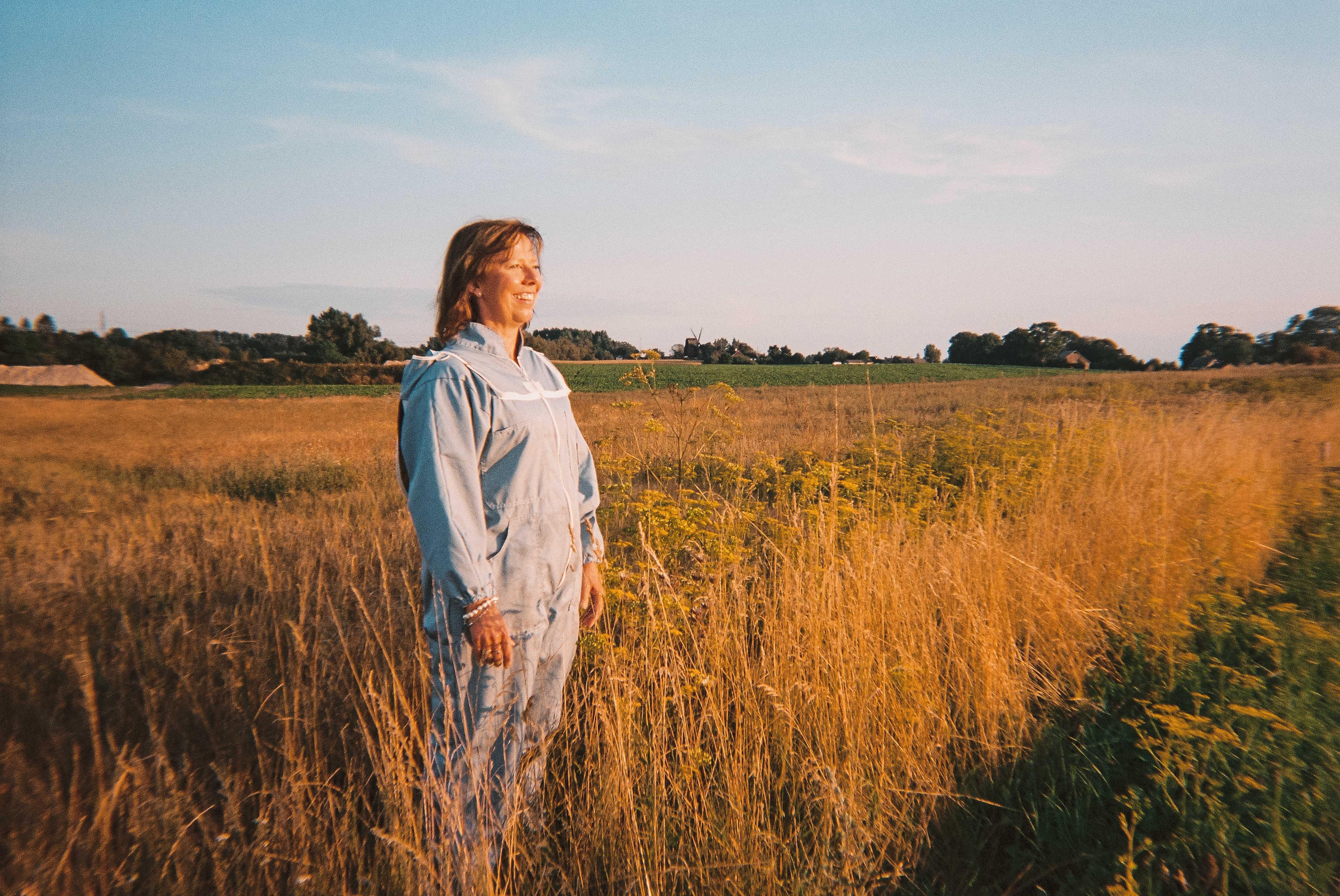 Biodlare i skyddsdräkt i naturlig bigård vid blommande äng, ekologisk honung